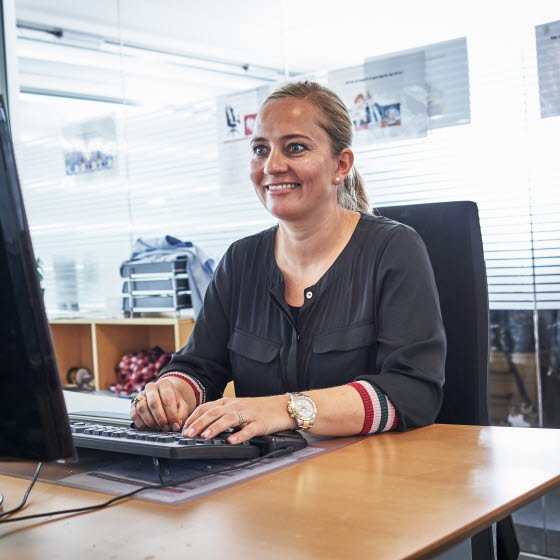 Smilende kvinde sidder på kontor foran computerskærm og tastatur