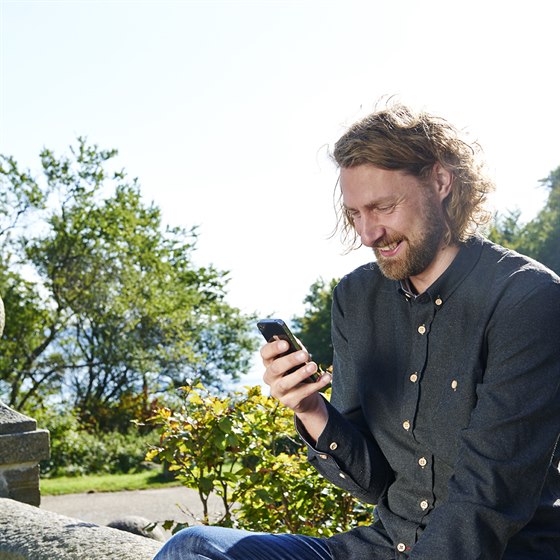 Ung mand sidder ude og kigger på mobiltelefon
