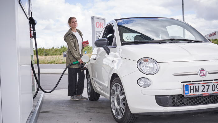 Kvinde tanker lille hvid bil på en OK-tankstation