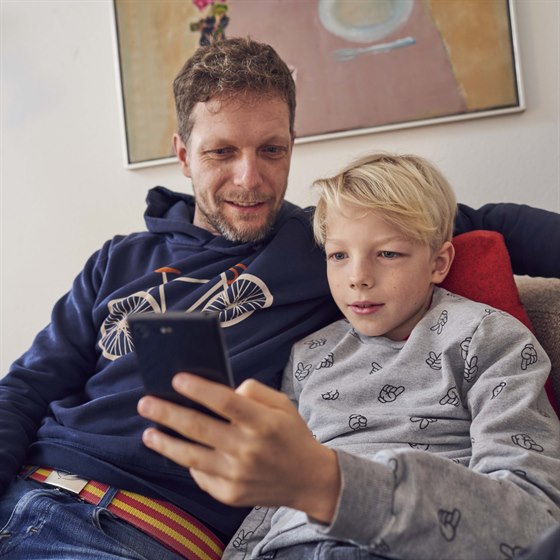 Far og søn sidder sammen i sofa og kigger på en mobiltelefon