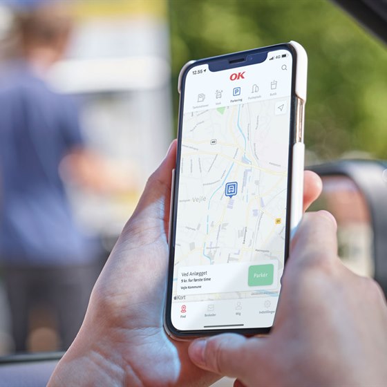 Kvindehånd holder telefon med parkering i OK-appen