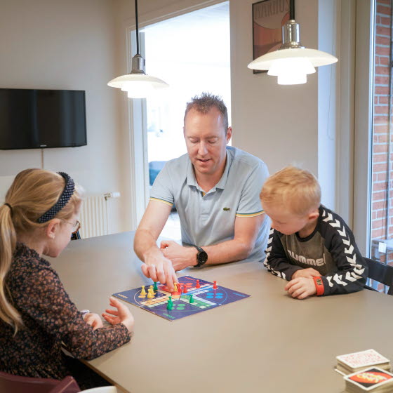 Far med to børn spiller ludo ved spisebord