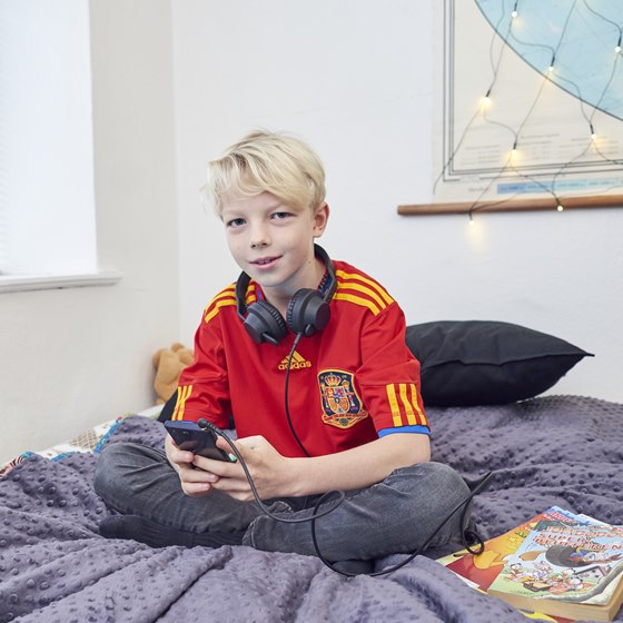 Dreng sidder på seng med mobiltelefon og headset
