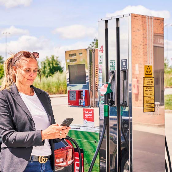 Kvinde tanker bilen mens hun står med sin telefon
