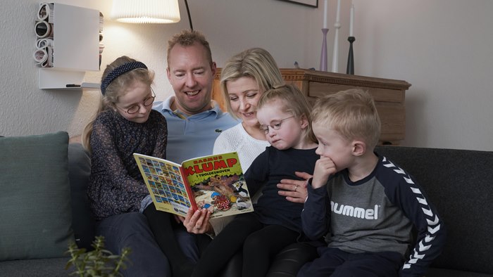 Familie sidder i sofahjørnet og læser Rasmus Klump-bog sammen