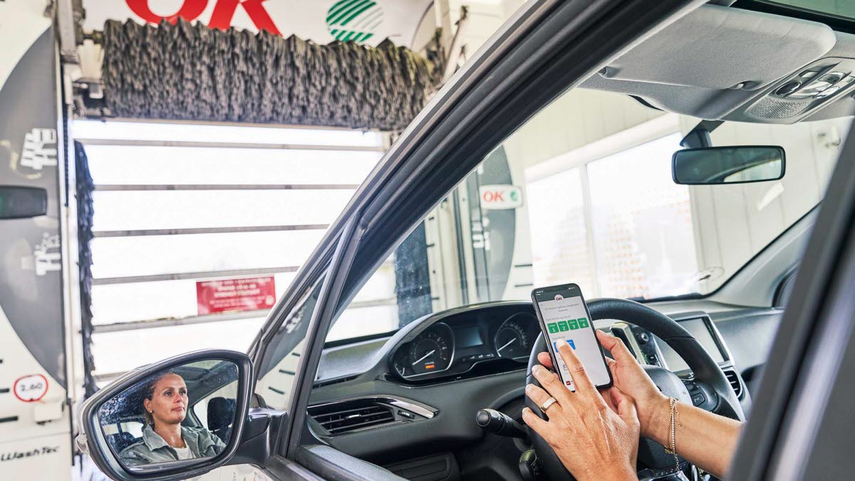 Kvinde sidder i bil i vaskehal med sin telefon