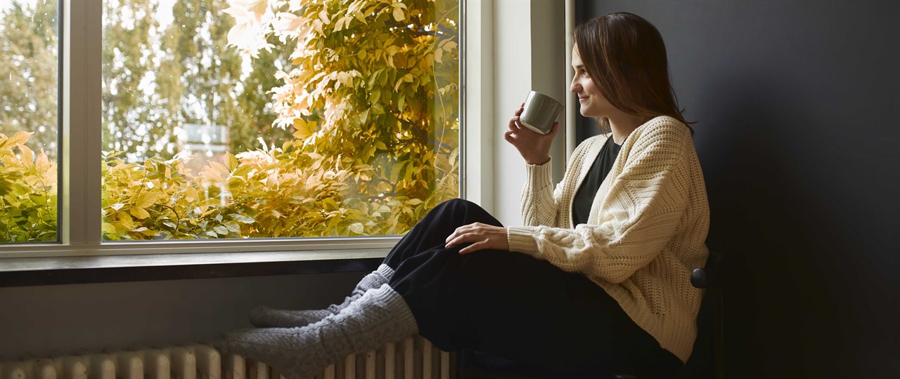 Kvinde sidder i vindueskarm med fødder på radiator