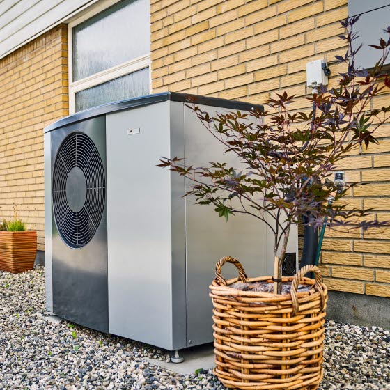 Varmepumpe står i grus foran et gult murstenshus