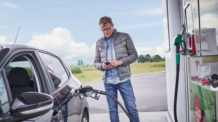 Mand tanker brændstof på OK-tankstation mens han holder sin mobiltelefon