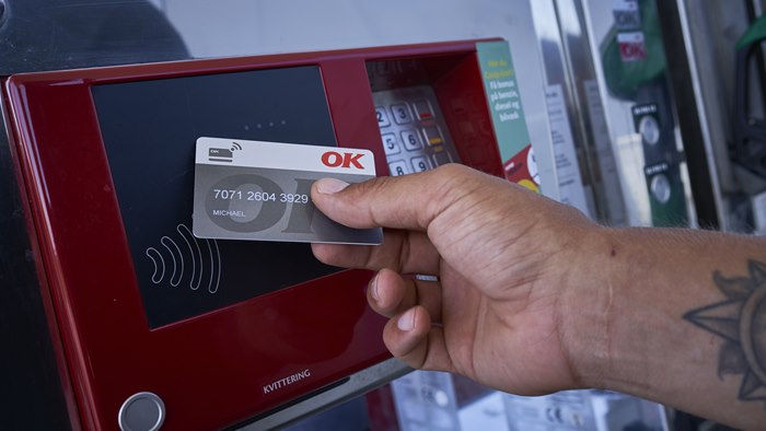 Hånd med et OK Erhvervskort ved en af OK's kontaktfri betalingsautomat