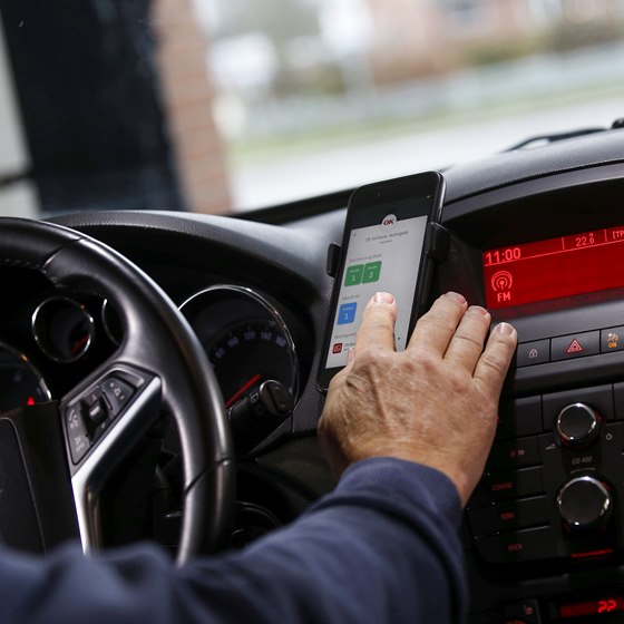 Førerkabine i bil med hånd på mobiltelefon i færd med at vælge bilvask med OK's app