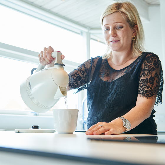 Kvinde hælder vand fra elkedel op i en kop