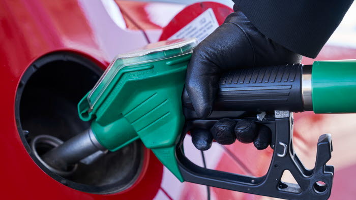 Hånd iført handske med tankpistol i færd med at påfylde brændstof på rød bil
