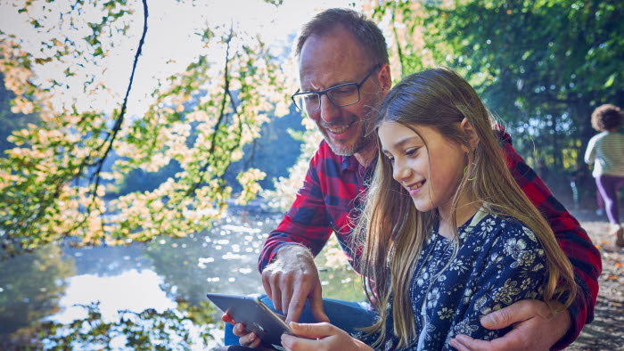 Far og datter i skoven sidder med tablet