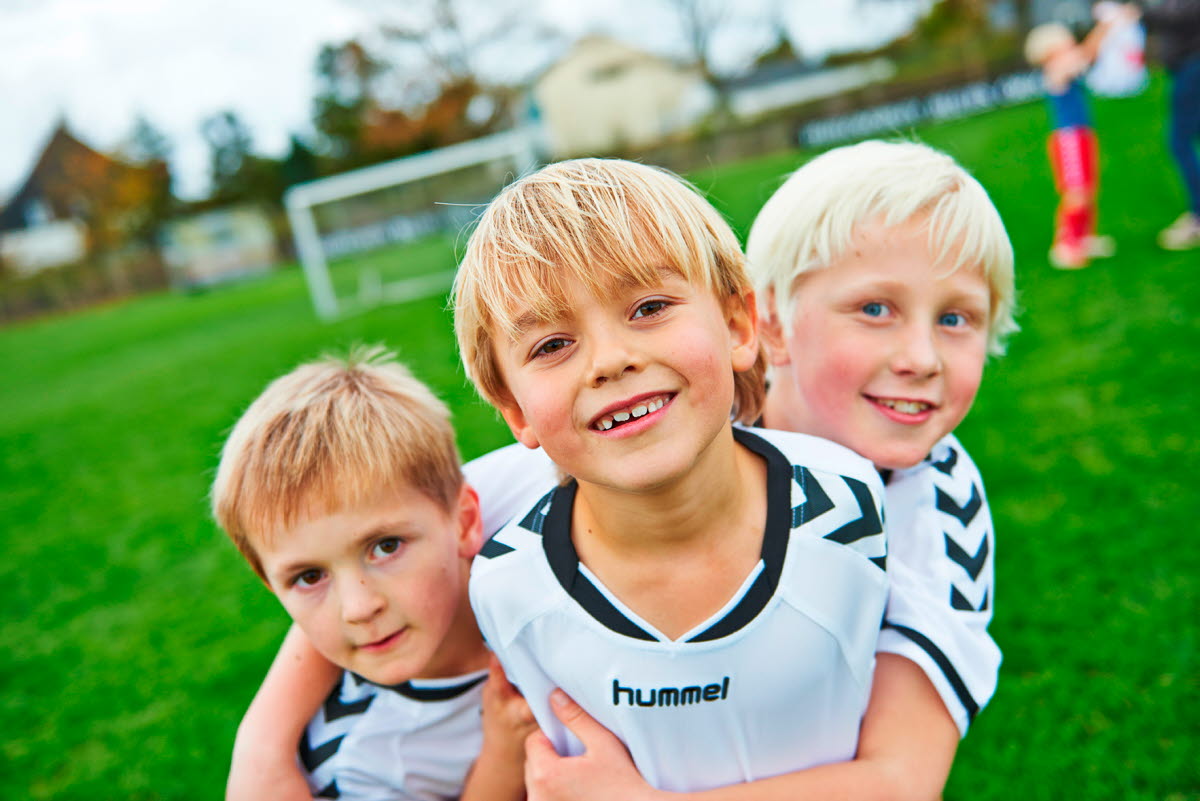 Tre fodbolddrenge iført OK fodboldtrøjer