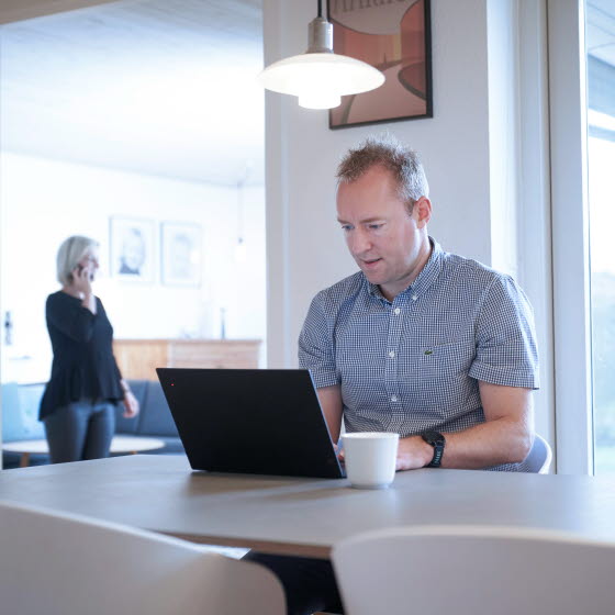 Mand sidder med bærbar computer ved spisebord