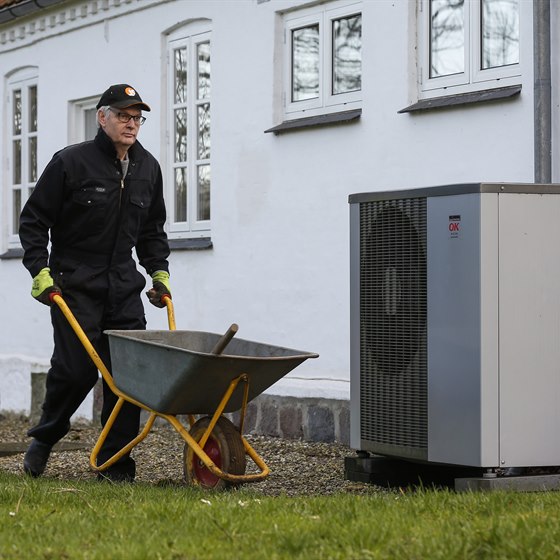 Mand med trillebør går foran hus med en luft til vand-varmepumpe