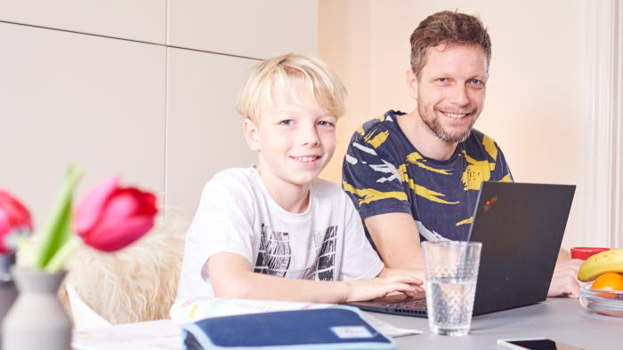 Far og søn ved spisebord med PC og penalhus foran sig