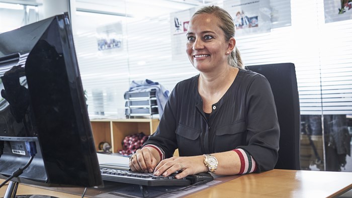 Smilende kvinde sidder på kontor foran computerskærm og tastatur