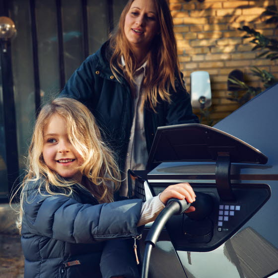 Pige med ladestik til elbil i hånden ved siden af bilen