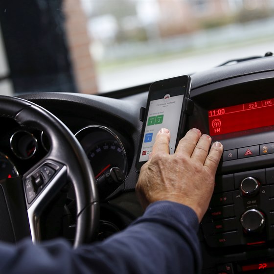 Førerkabine i bil med hånd på mobiltelefon i færd med at vælge bilvask med OK's app