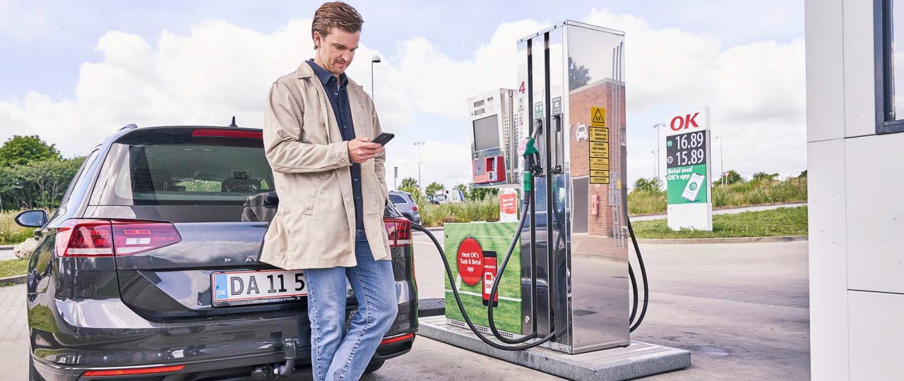 mand står op af sin bil på tanken med sin telefon