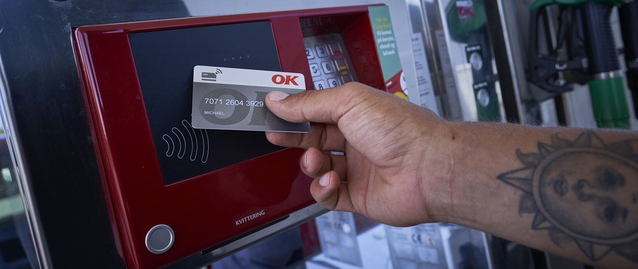 Hånd med et OK Erhvervskort ved en af OK's kontaktfri betalingsautomat