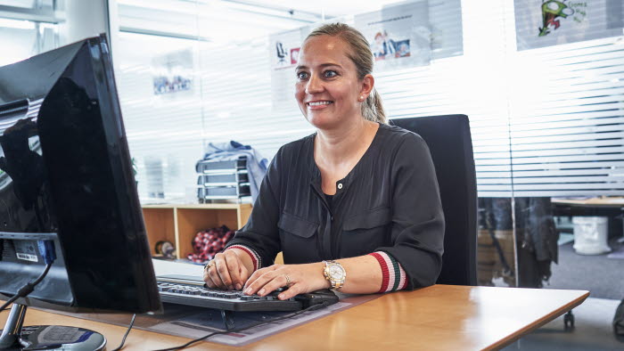 Smilende kvinde sidder på kontor foran computerskærm og tastatur