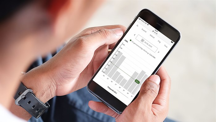 Mand sidder med mobiltelefon og tjekker elforbrug på selvbetjeningen Min OK
