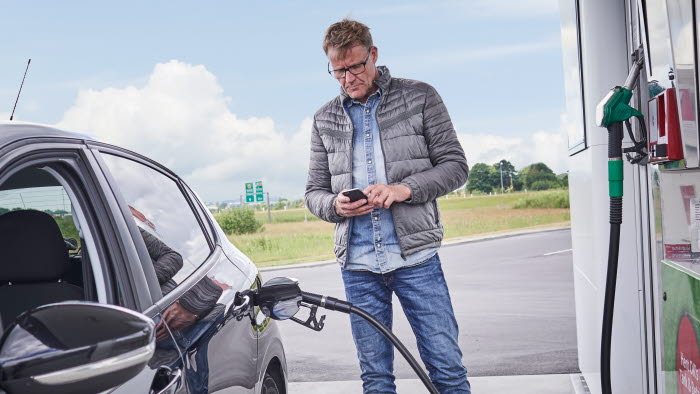 Mand tanker brændstof på OK-tankstation mens han holder sin mobiltelefon