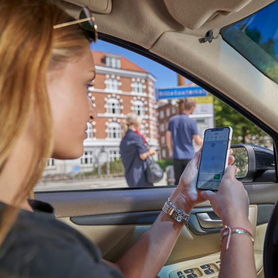 Kvinde sidder i bil med OK's app på smartphones app