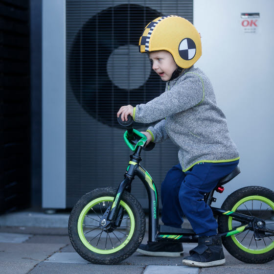 Lille dreng på sin cykel foran en varmepumpe