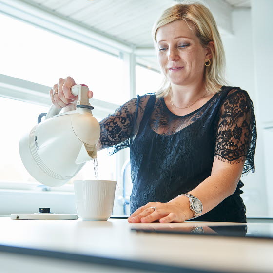 Kvinde hælder vand fra elkedel op i en kop